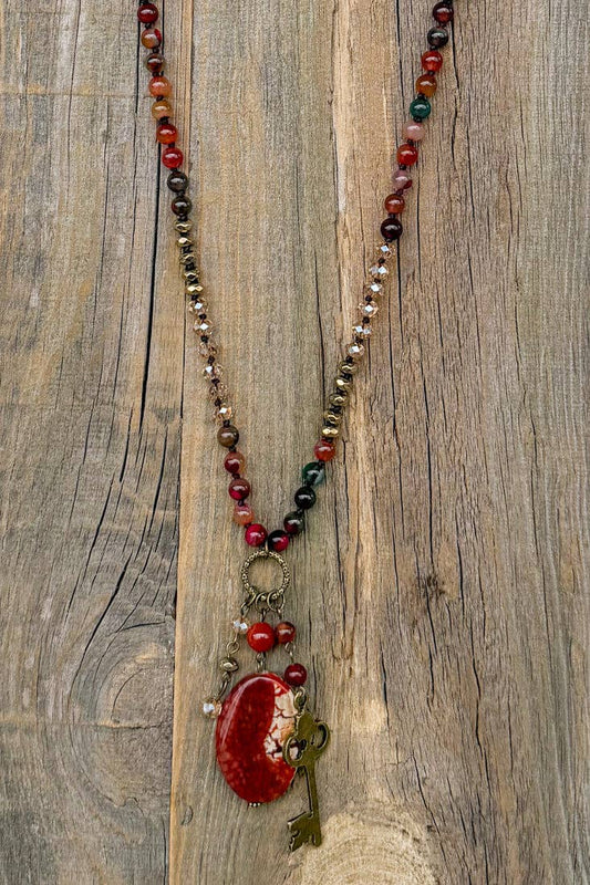 Suki necklace hanging on wood, showing the full length and red fire agate pendant