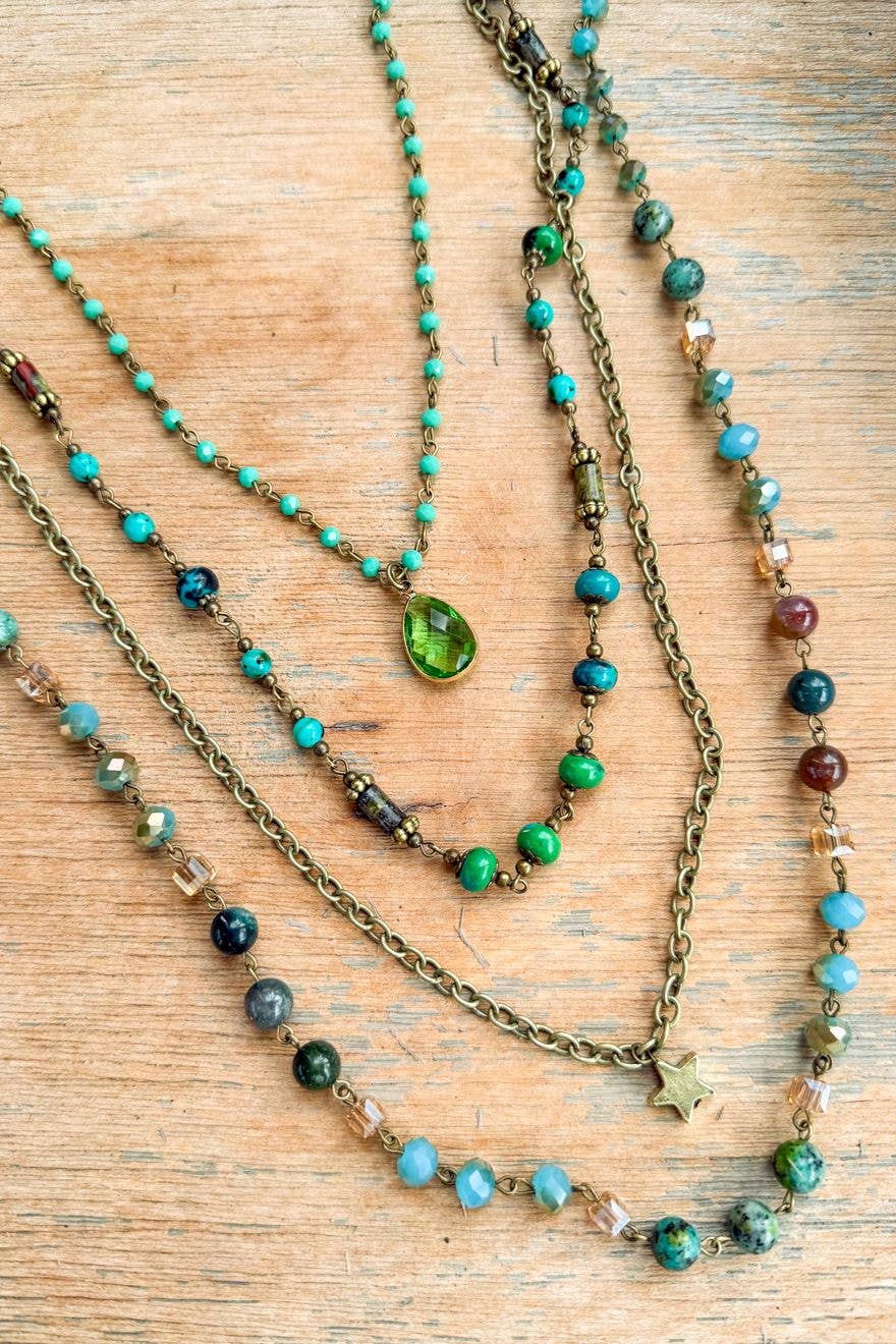 Santorini layered necklace on wood, showing the teardrop pendant and star charm
