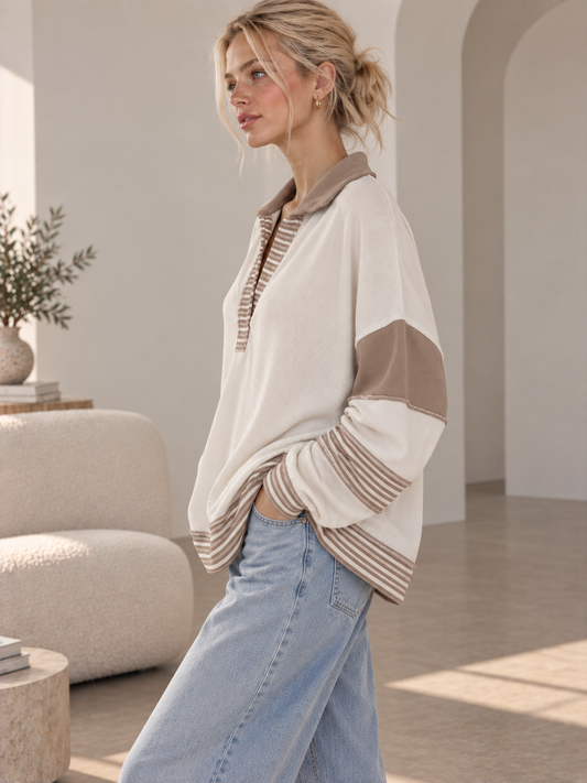 Woman in a cream French terry polo collar top with tan contrast sleeve panels and striped trim, side view