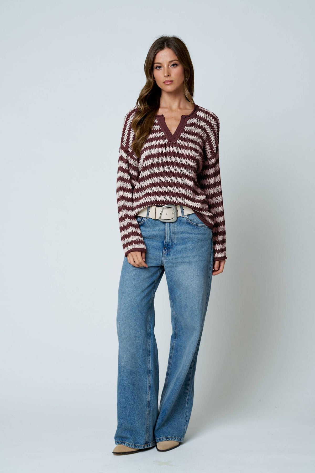 Full length view of the burgundy striped sweater styled with wide leg jeans and a white belt