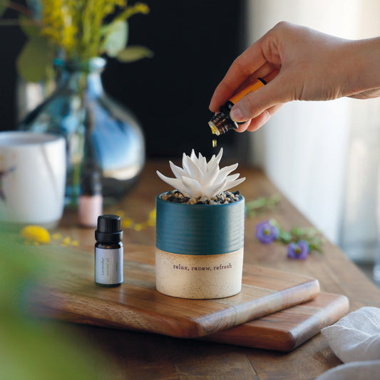 Hand dripping essential oil onto the white succulent diffuser on a wooden board