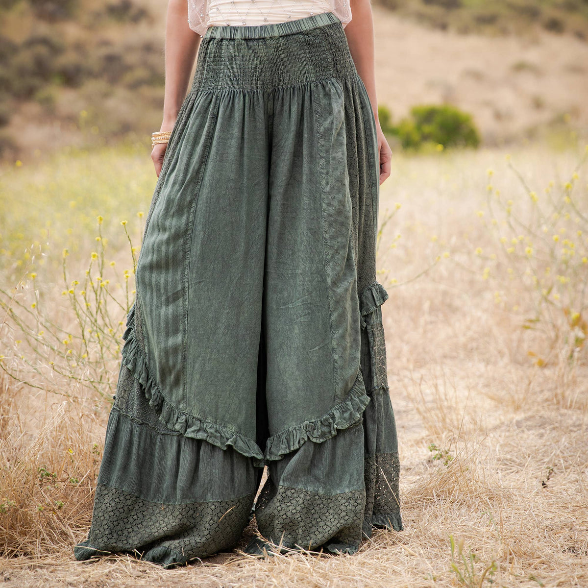 Front view of the basil green smocked waist pants with lace panels and tiered ruffles