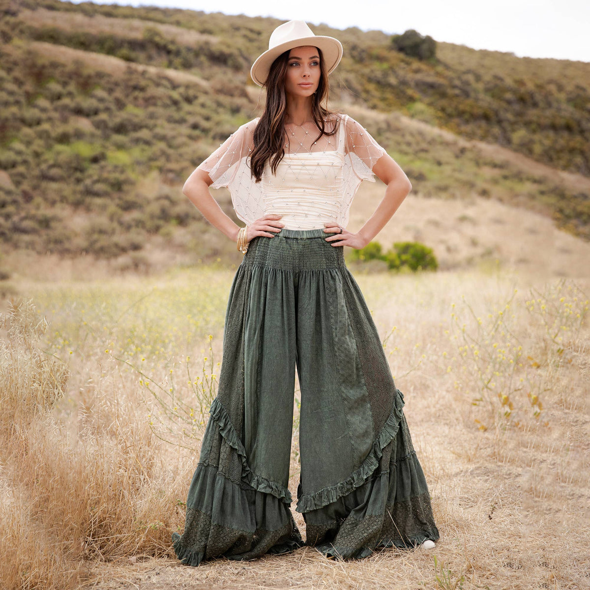 Woman in a white lace top and straw hat wearing the basil wide leg ruffle pants, hands on hips
