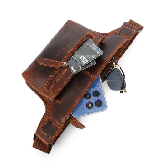 Chestnut leather belt bag with front zip pockets holding a phone and sunglasses