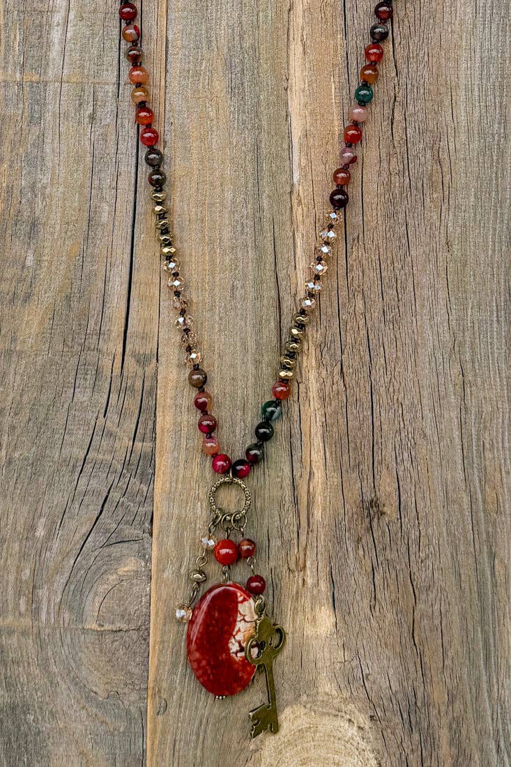 Suki necklace hanging on wood, showing the full length and red fire agate pendant