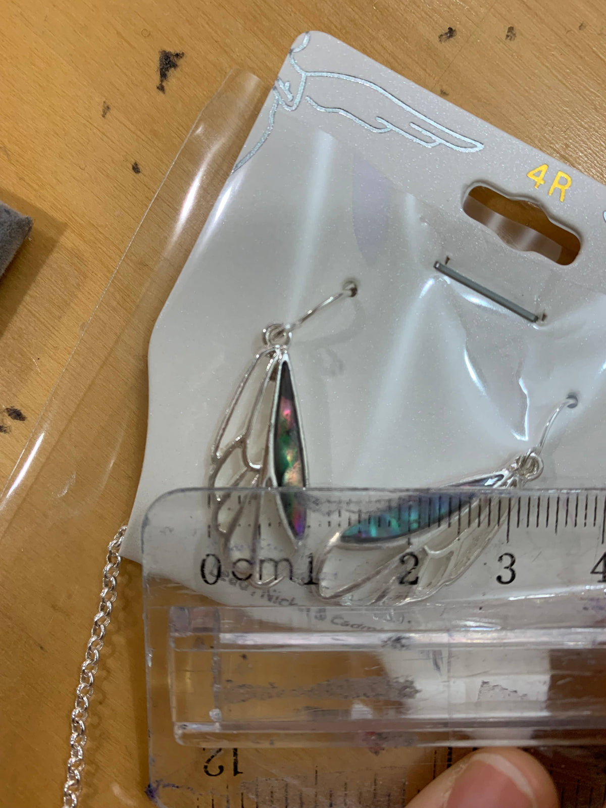 Dragonfly wing earrings on the display card beside a ruler