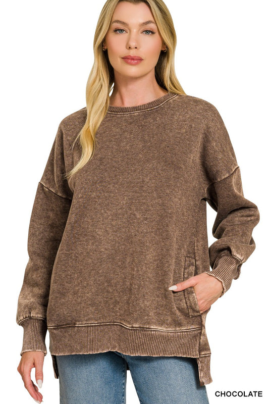 Model in an oversized chocolate brown acid wash fleece pullover with a hi-low raw hem and side seam pockets, worn with jeans