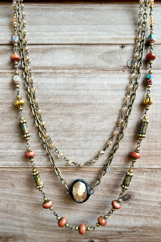 Justina layered necklace with red jasper and earthy beads and an oval pendant, on wood