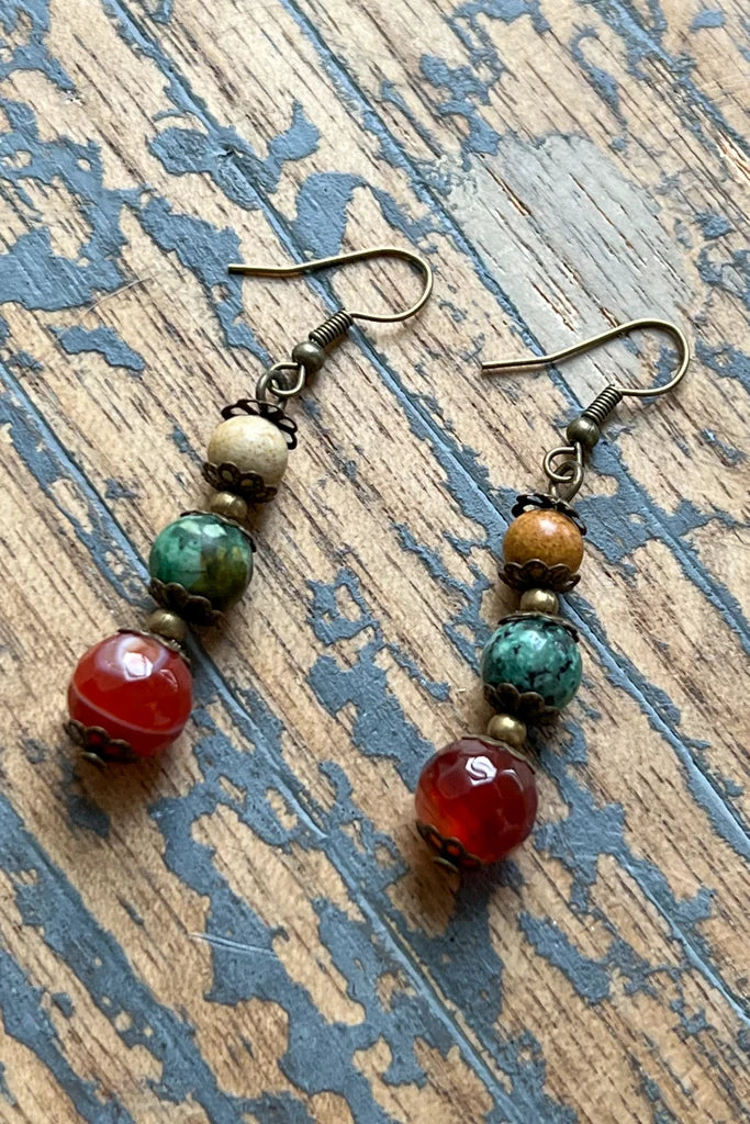 Austin bronze dangle earrings with cream, green and carnelian red stone beads on distressed blue wood
