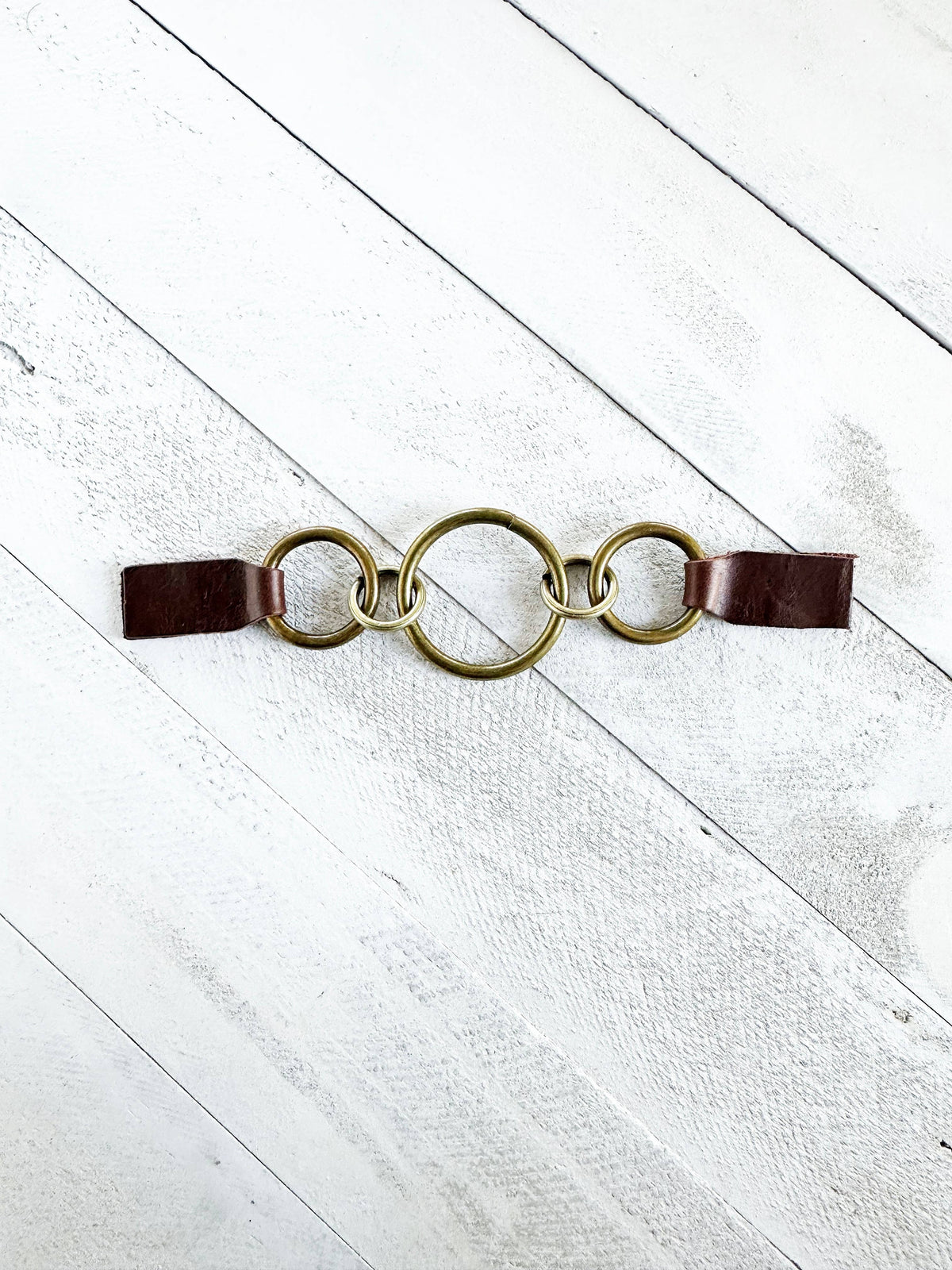 Three interlocking bronze rings with dark brown leather grip tabs on white wood