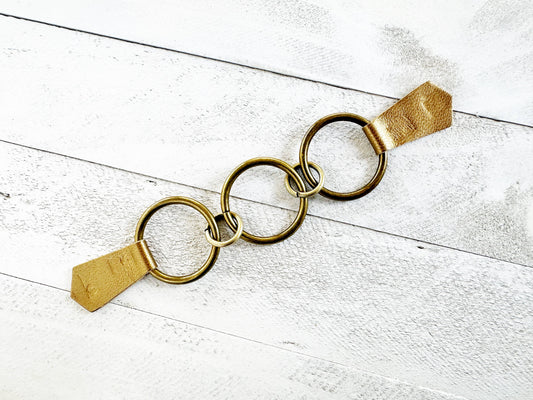 Three interlocking bronze rings with metallic gold leather tabs on white wood