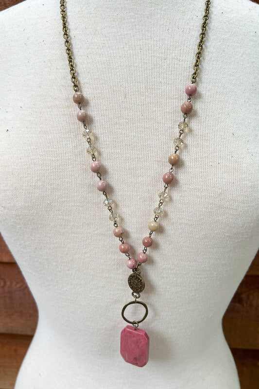 Long chain necklace with mauve pink beads and a pink polished agate pendant on a display bust