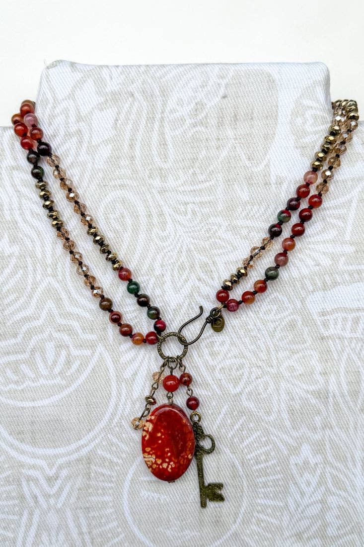 Long beaded necklace in red, green and brown with a red fire agate pendant and a bronze key charm
