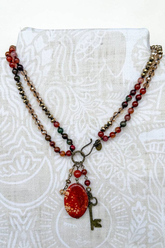 Long beaded necklace in red, green and brown with a red fire agate pendant and a bronze key charm