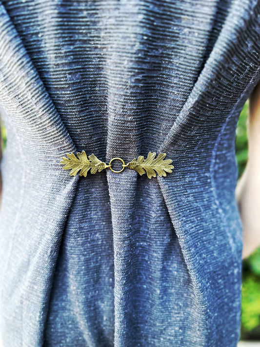 Bronze oak leaf cloak clasp cinching the back of a blue knit dress, outdoors