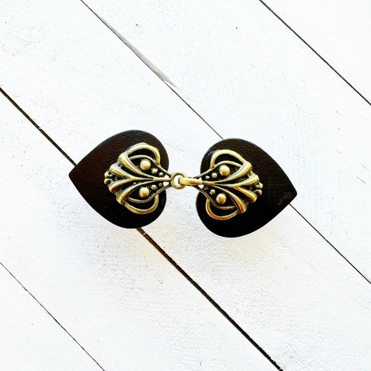 Dark brown leather heart cinch clip with antique bronze filigree, closed, on white wood