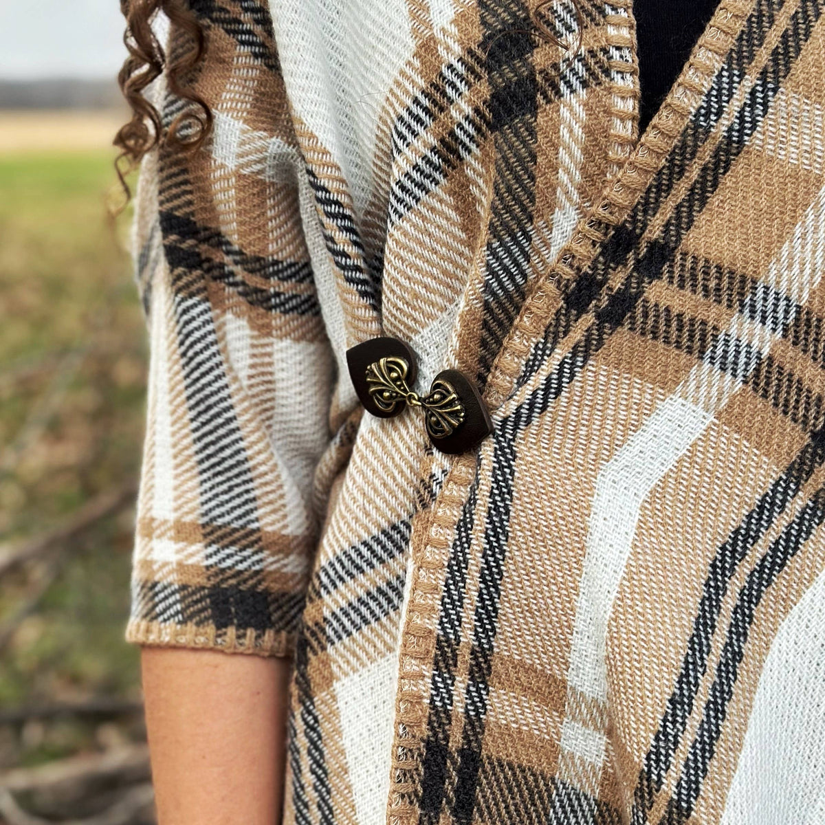 Dark brown and bronze cinch clip gathering a tan plaid poncho at the shoulder
