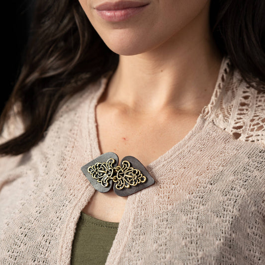 Wide dark brown leather clasp with sprawling bronze filigree closing a cream open-knit cardigan