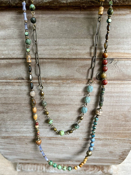 Two-layer necklace with a bronze beaded chain and an earthy beaded strand, on wood