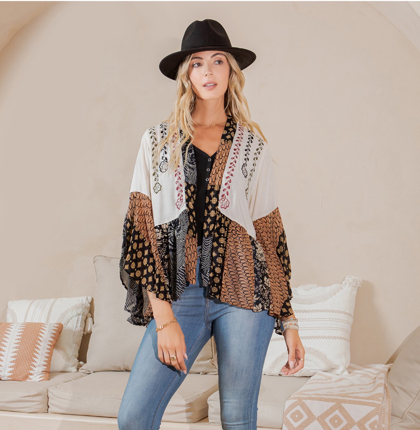Model in an open-front pearl shrug with aari embroidery and brown patchwork flared sleeves, styled with jeans and a black hat
