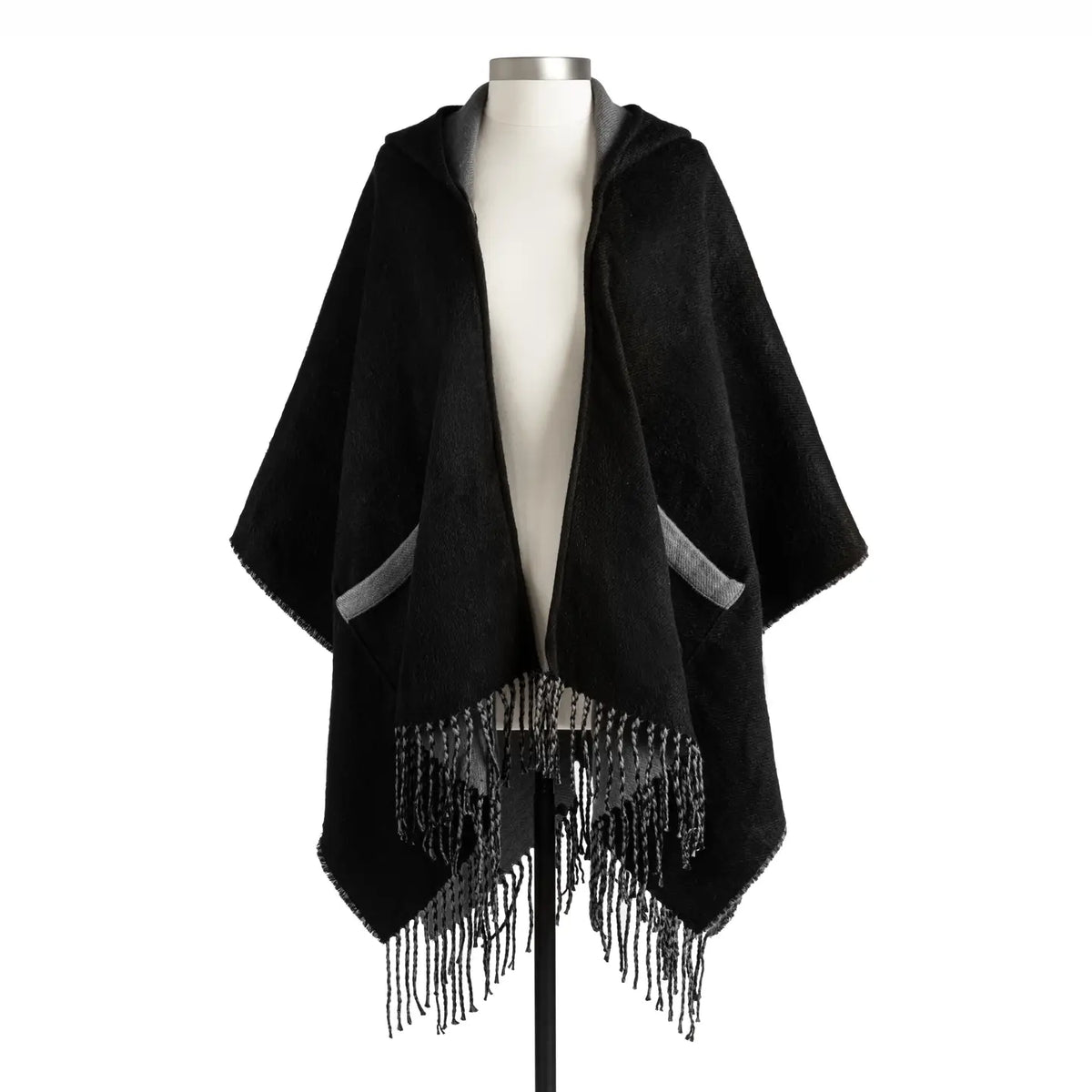 Black hooded ruana wrap displayed open on a dress form, showing the two front patch pockets and the long fringed hem