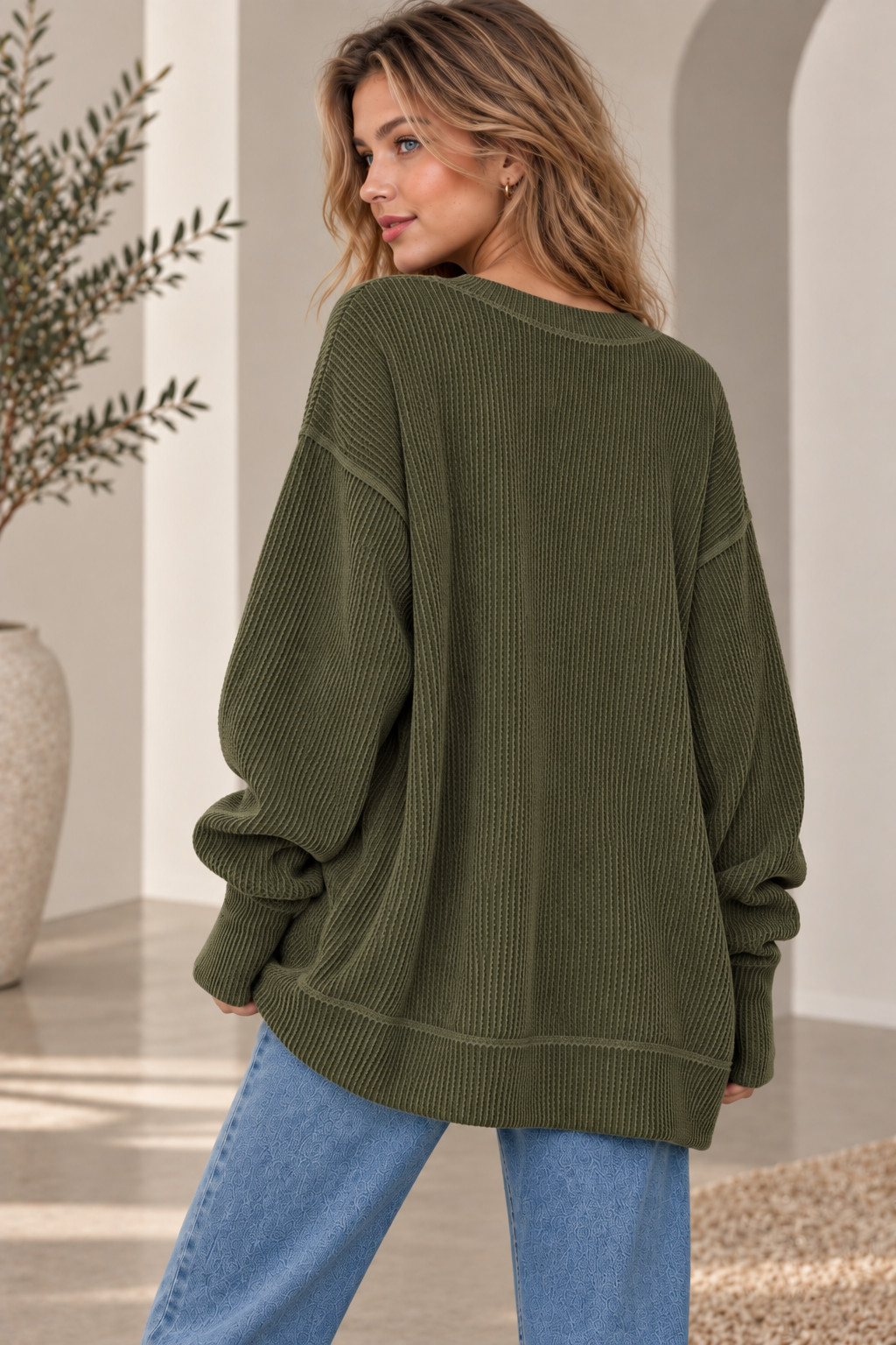 Woman in an oversized olive ribbed knit crewneck sweatshirt with jeans, back view