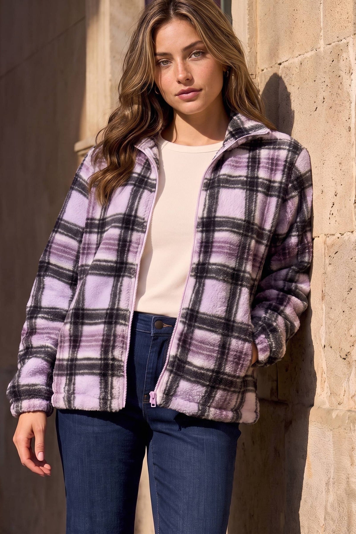 Woman wearing the violet and black plaid teddy zip-up jacket open over a cream top and jeans