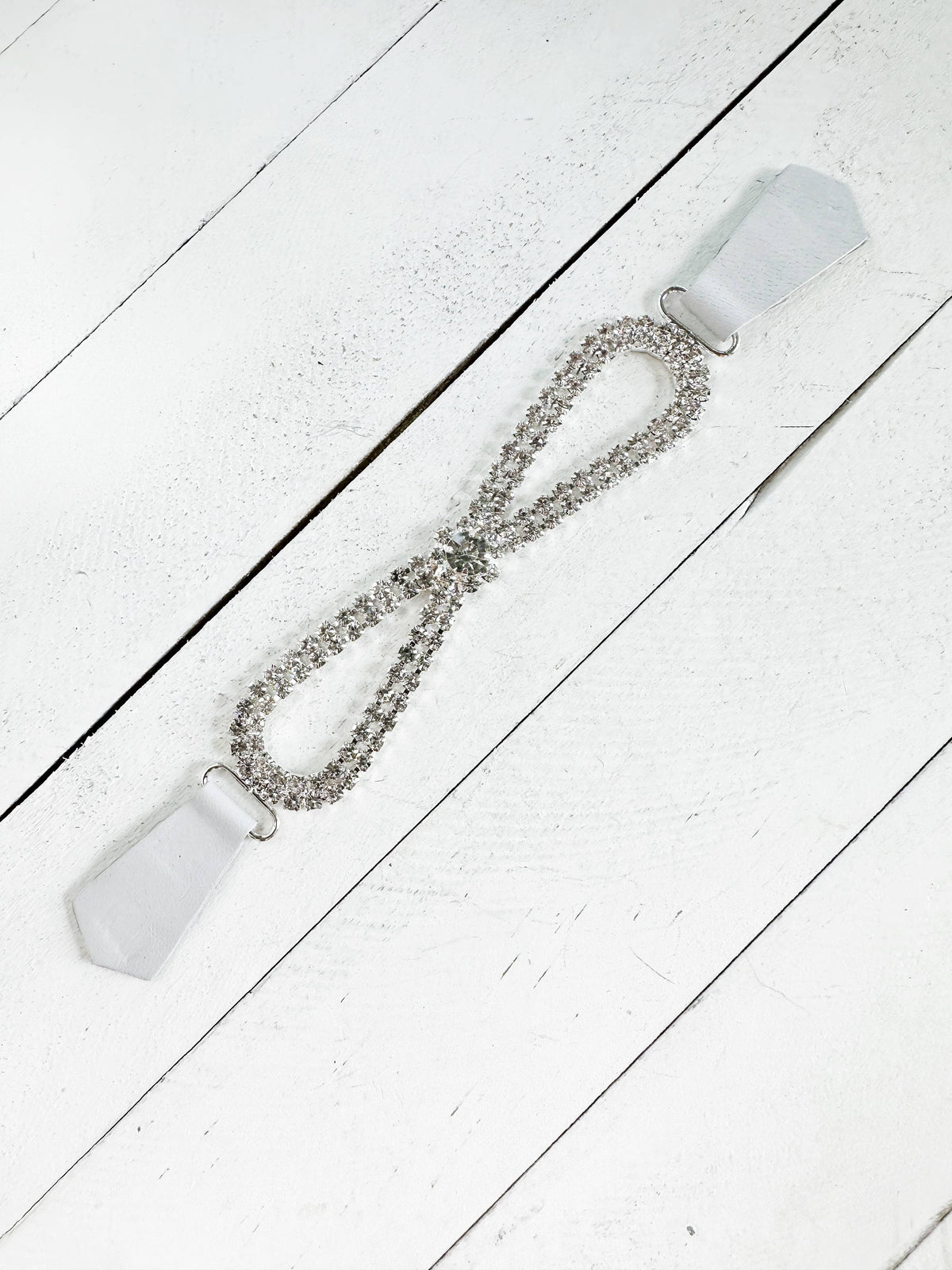Rhinestone infinity-loop cinch clip with white leather tabs, flat on white wood