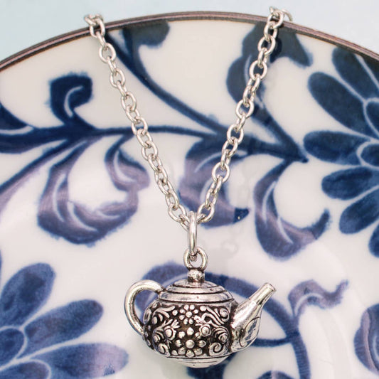 Silver teapot pendant necklace on a blue and white floral plate