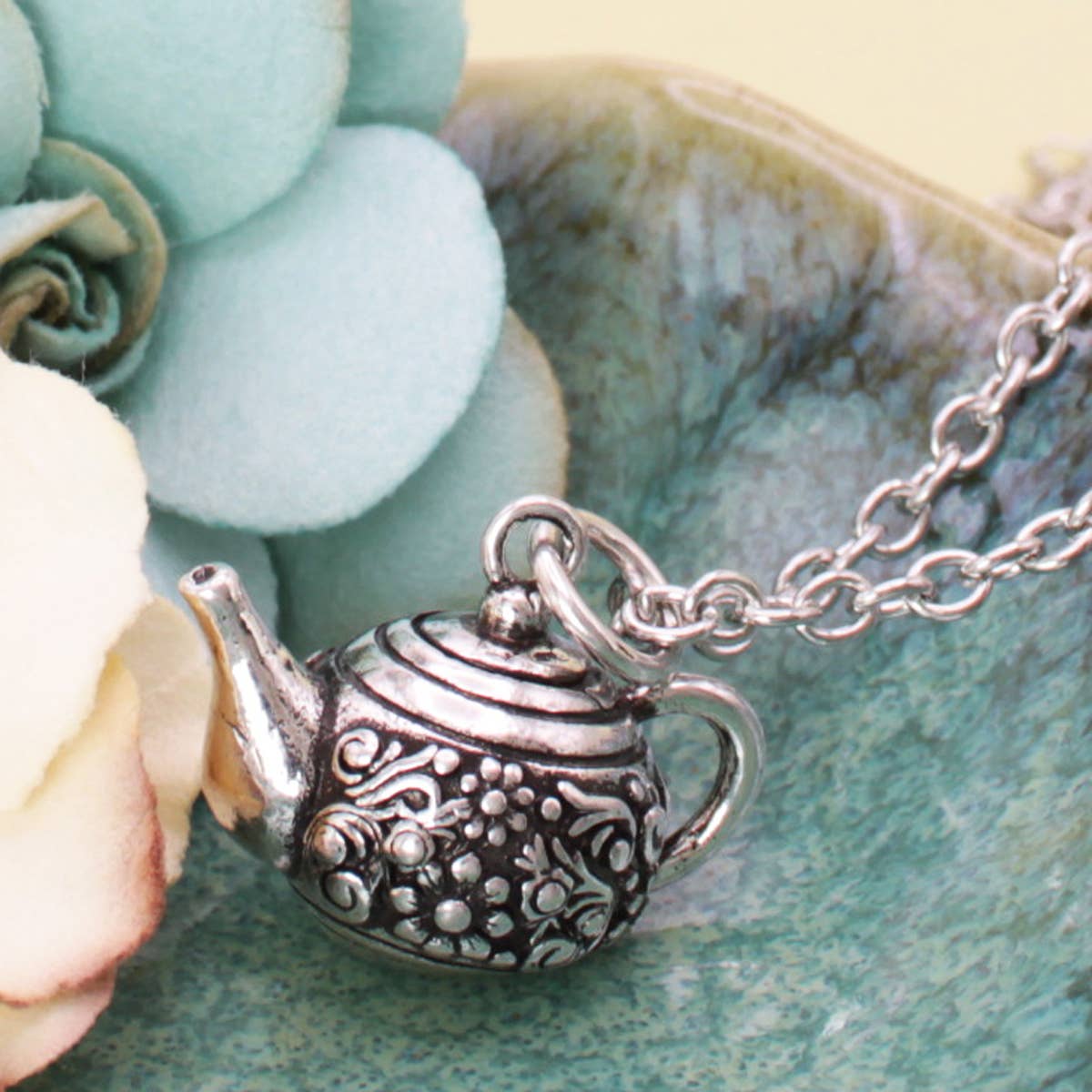 Close-up of the floral etched silver teapot pendant resting in a shell