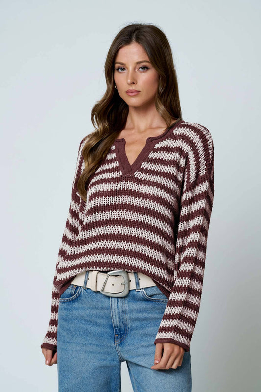 Model in a burgundy and cream striped sheer knit sweater with a split V neck, worn with jeans and a white belt, front view