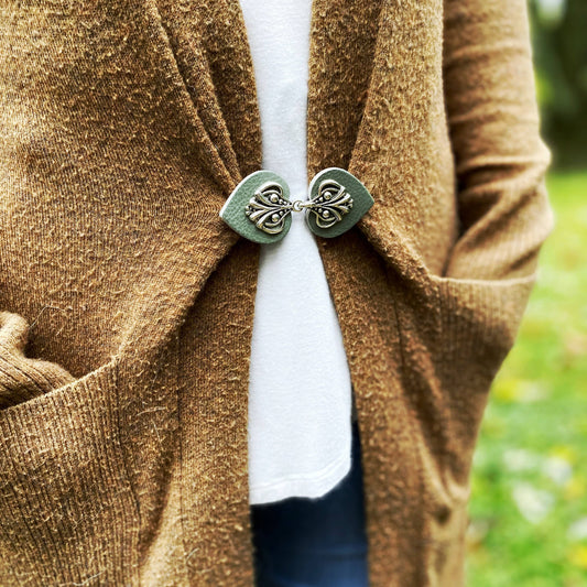 Sea green leather cinch clip with silver filigree holding a camel cardigan closed