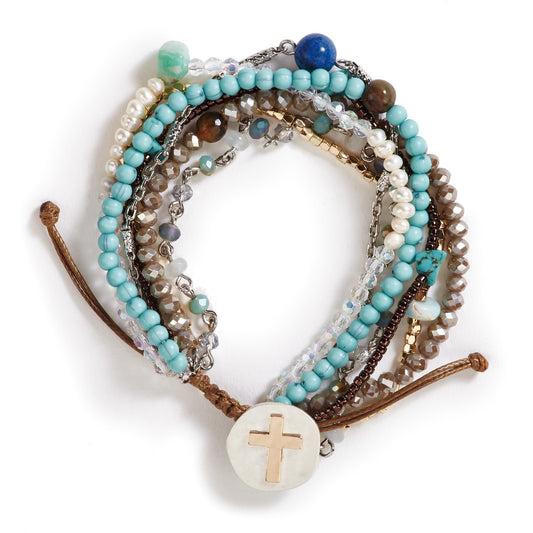 Your Journey prayer bracelet in turquoise laid flat, seven beaded strands in aqua and wood tones gathered to a mother of pearl cross disc with a leather pull tie